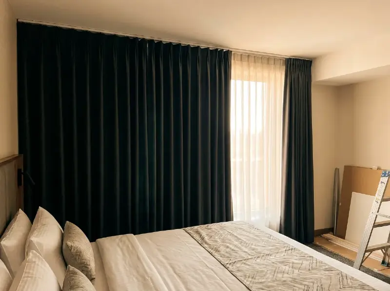 Zware verduisterende gordijnen op een rail in een hotelkamer, met de inbetween ernaast gehangen
