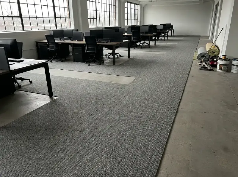 Grijs projecttapijt in banen gelegd in een open kantoorruimte, met de naden onzichtbaar tussen de werkplekken